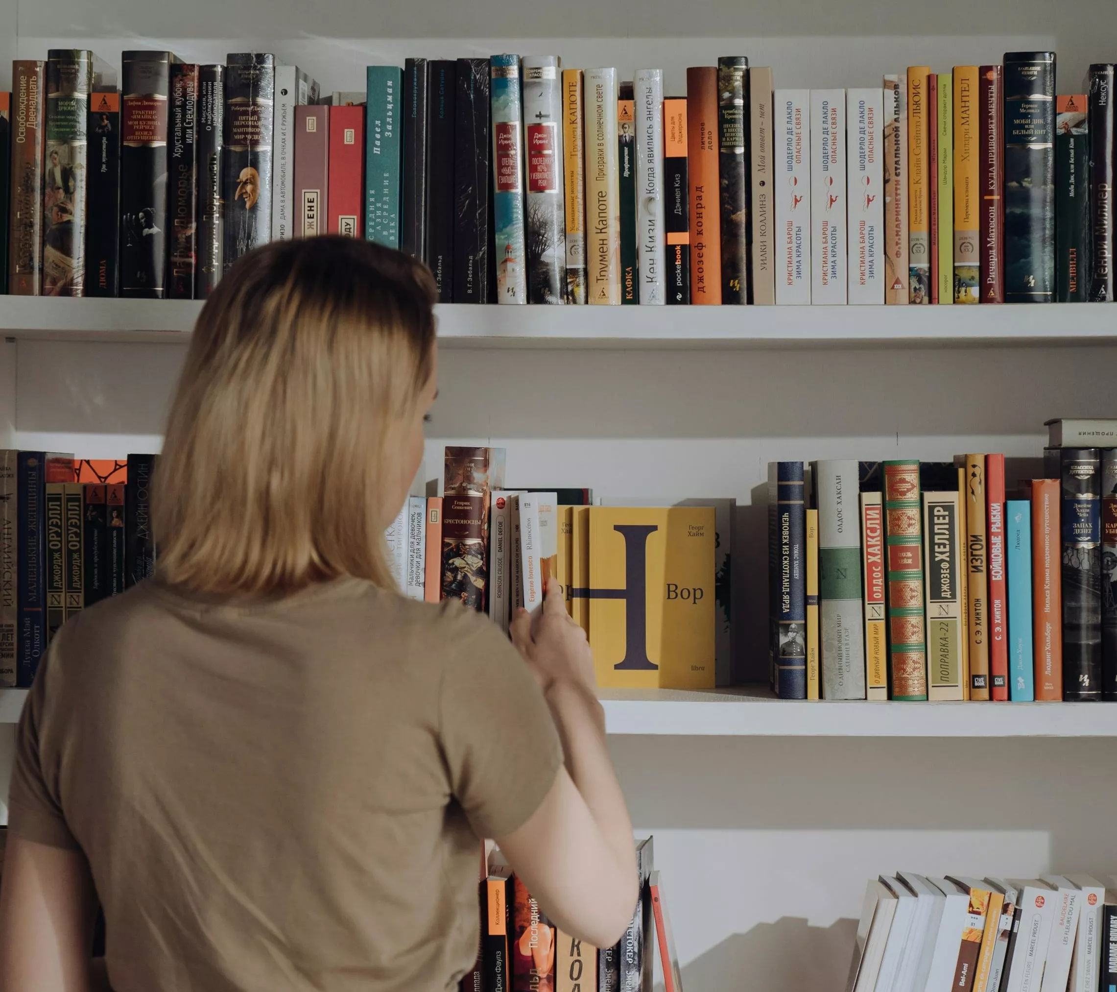 Photo of a person looking at a shelf full of books.